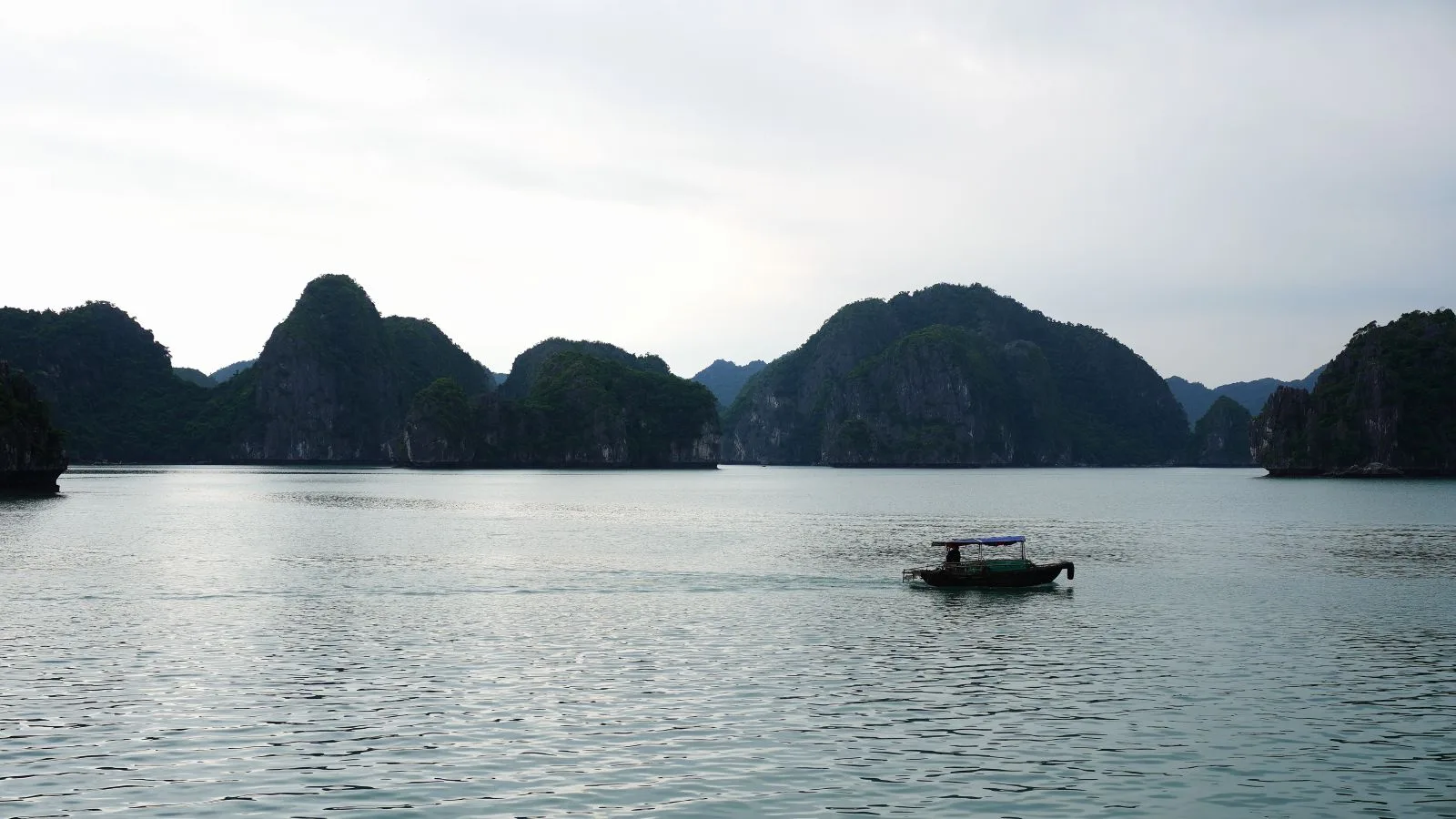 Barca local navegando por las aguas tranquilas de la bahía de Lan Ha con las islas kársticas de Cat Ba al fondo, en Vietnam