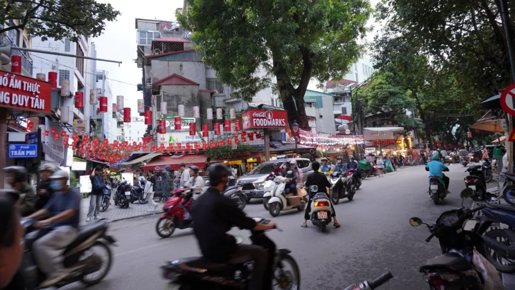 Calle del casco antiguo de Hanoi (Old Quarter) con motos, puestos callejeros y ambiente caótico típico de la ciudad.